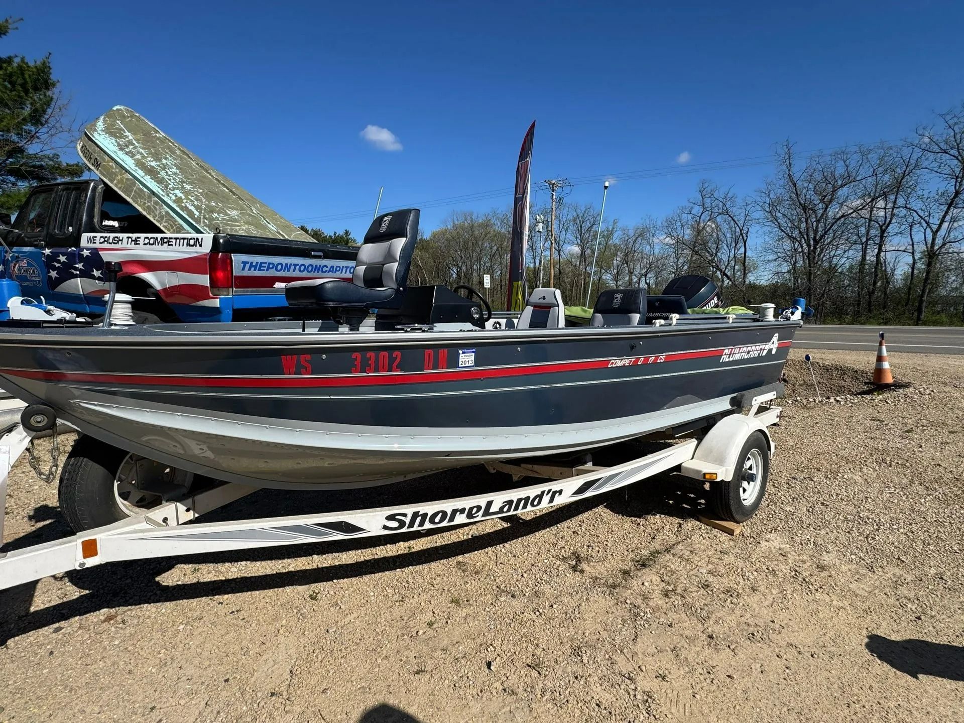 Black-and-silver fishing boat on trailer in a gravel lot under a clear blue sky