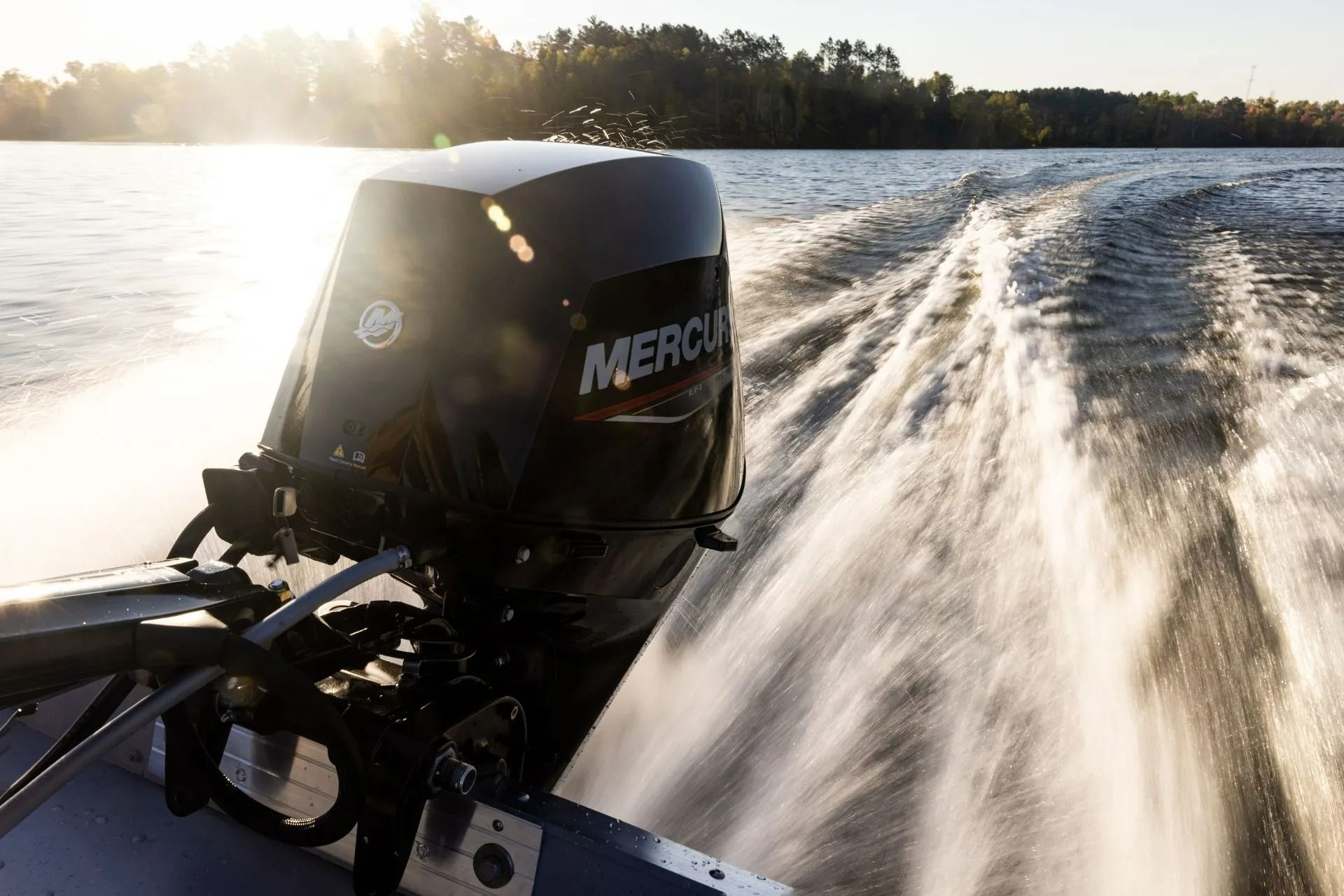 Boat racing on a lake, with a black Mercury outboard motor spraying white wake at sunset.