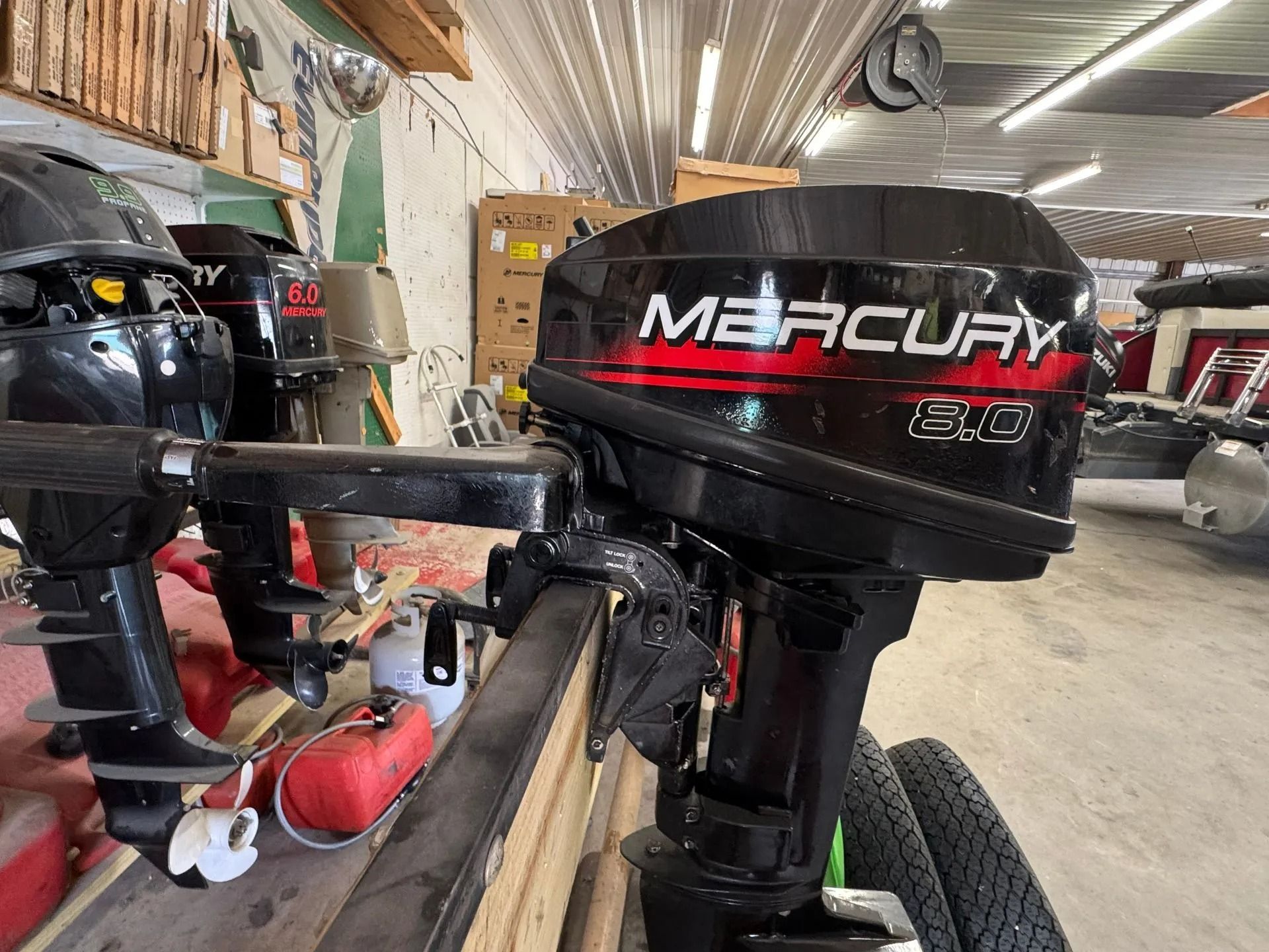 Mercury outboard motor mounted on a boat in a workshop, with other boats and tools nearby