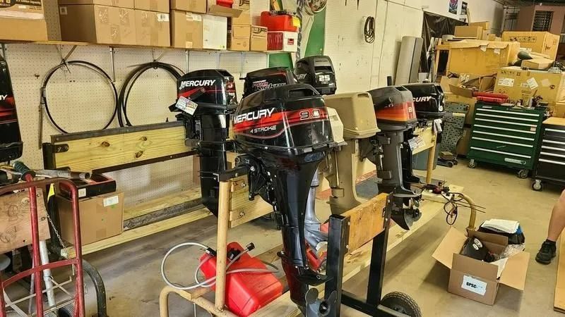 Workshop with several outboard motors on stands, shelves, tools, and boxes in the background