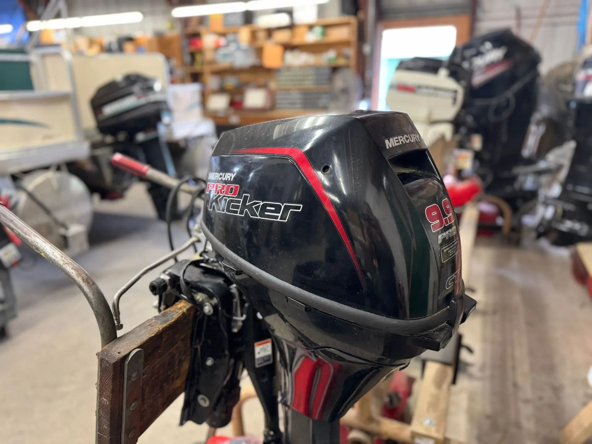 Black Mercury outboard motor mounted on a boat in a workshop, with another boat in the background