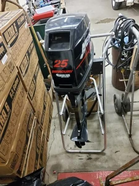 Black outboard motor on a metal stand in a workshop, surrounded by boxes and equipment.
