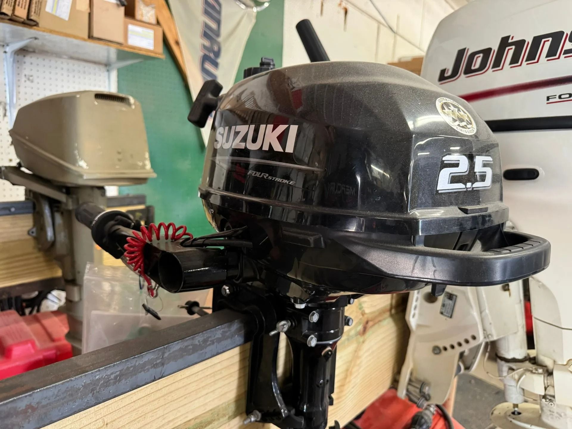 Suzuki 2.5 outboard motor mounted on a boat in a garage with other equipment nearby