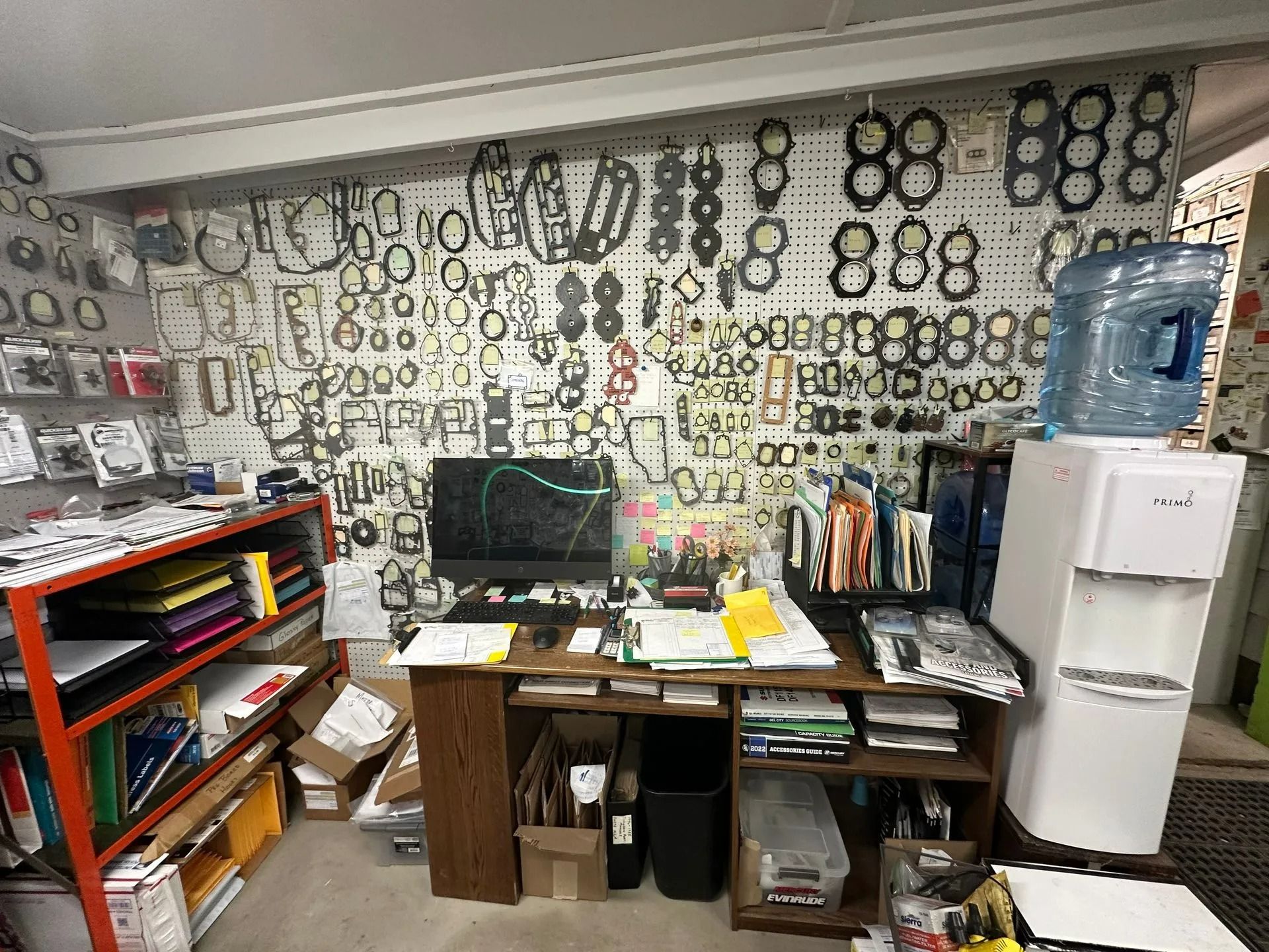 Workspace with a desk, computer, tools, and shelves, backed by a wall covered in circular patterns