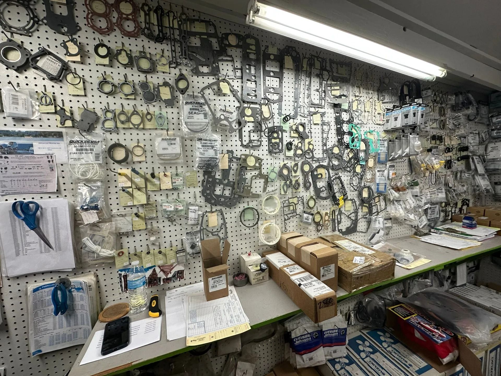 Wall of assorted hardware parts and tools above a cluttered workbench in a shop
