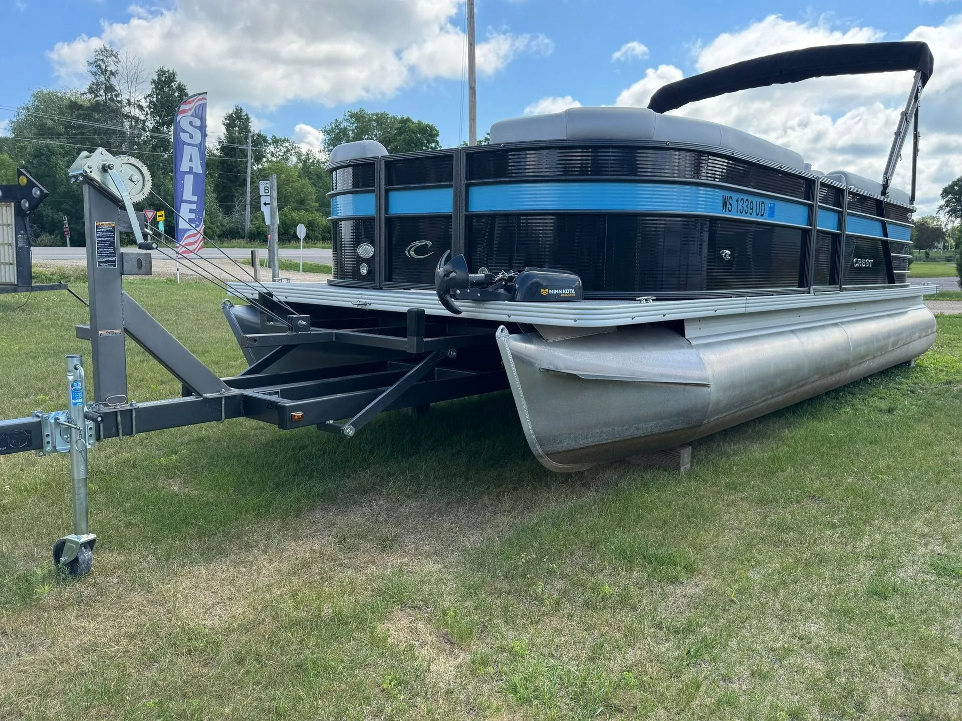 Pontoon boat with blue-and-black canopy parked on grass at an outdoor lot