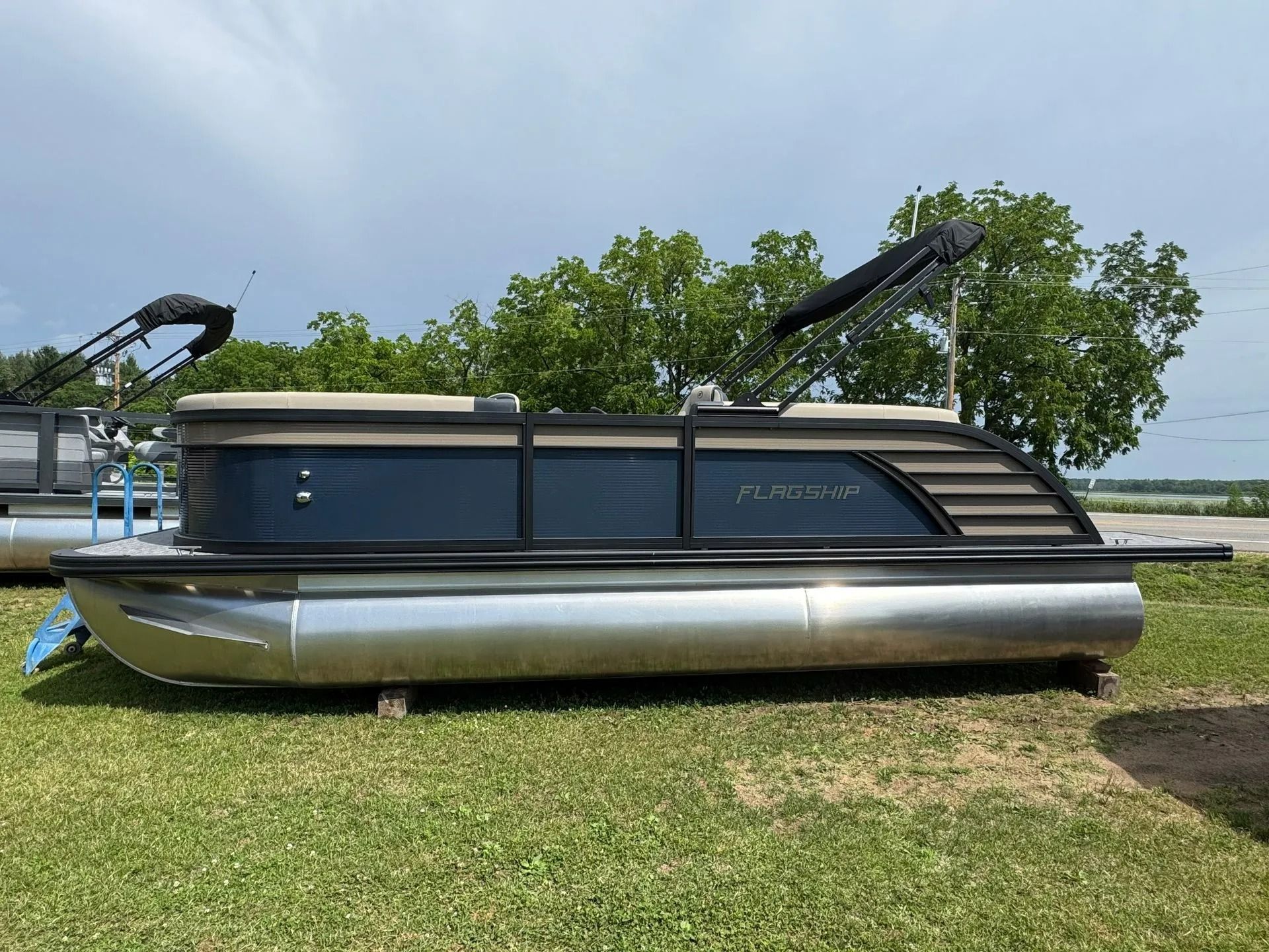 Pontoon boat with dark blue canopy and silver hull parked on grass near water