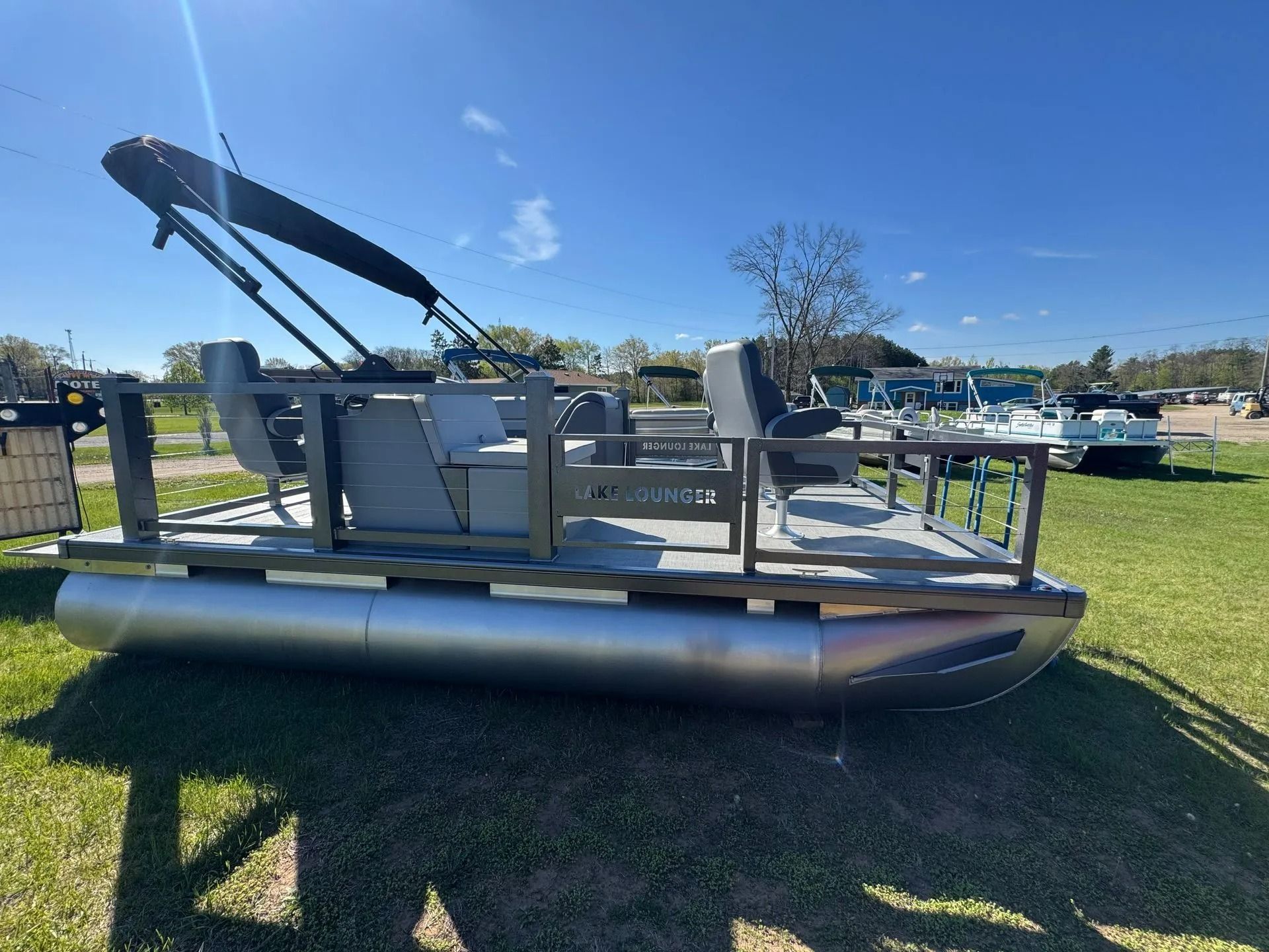 Pontoon boat with canopy on a grassy lot under a blue sky