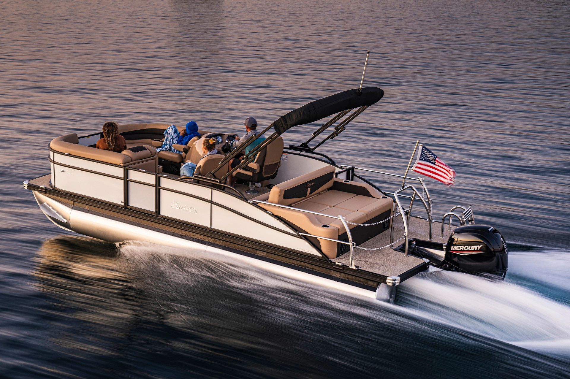 Pontoon boat speeding across blue water, stern view with twin outboard motors and wake behind.