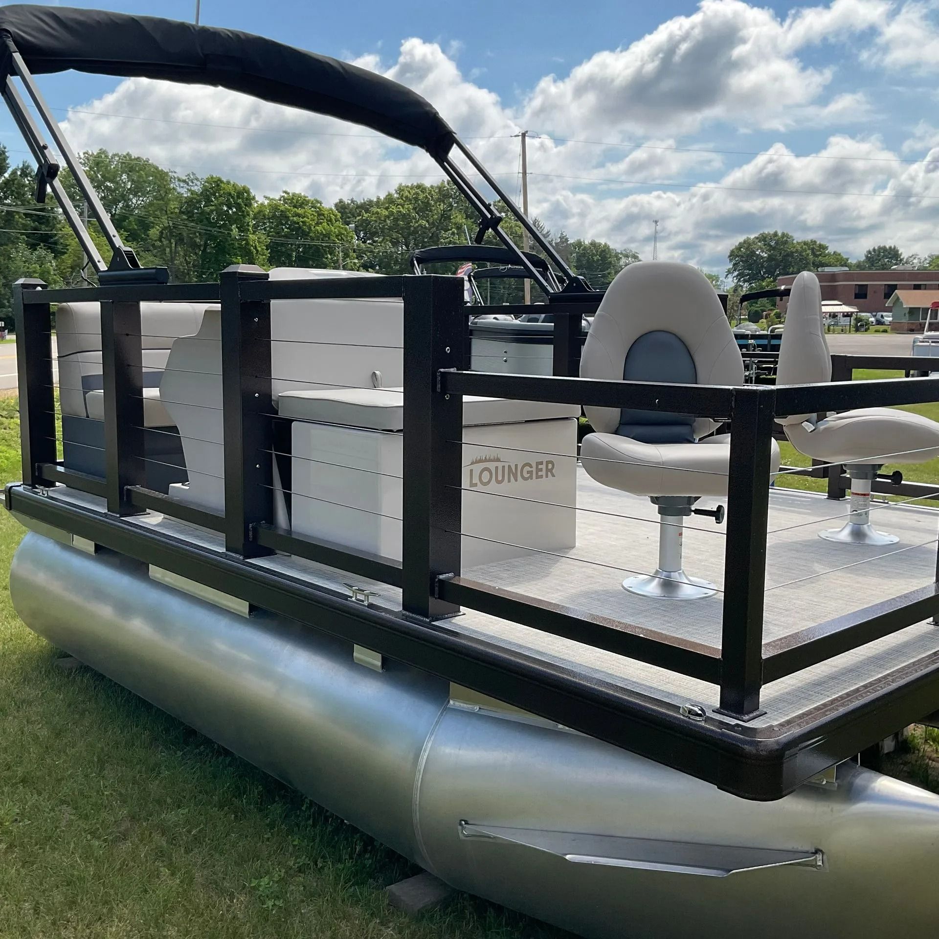Pontoon boat with black canopy and gray seats on grass under a cloudy sky