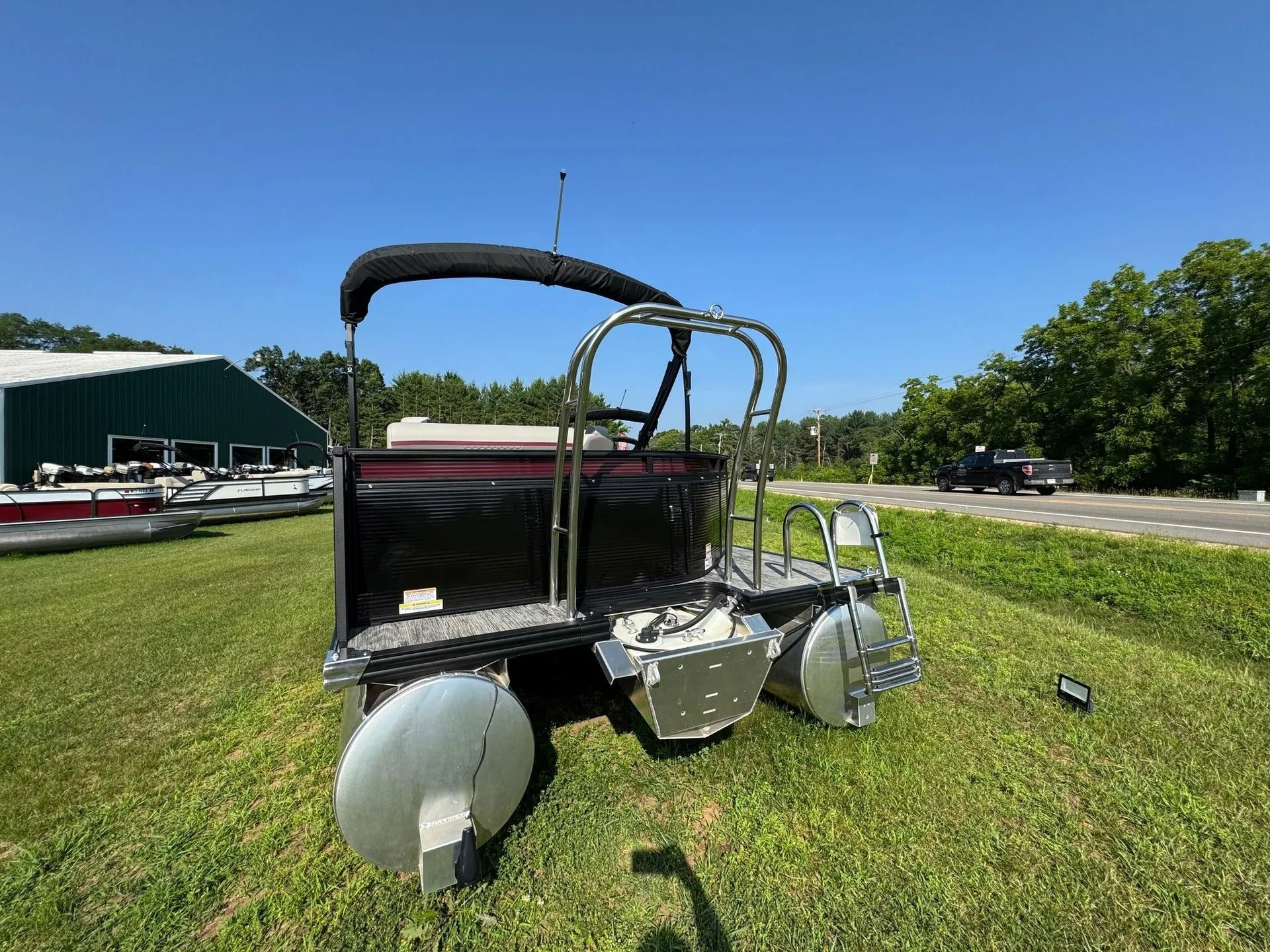 Small silver pontoon-style utility cart on grass beside a road under a blue sky