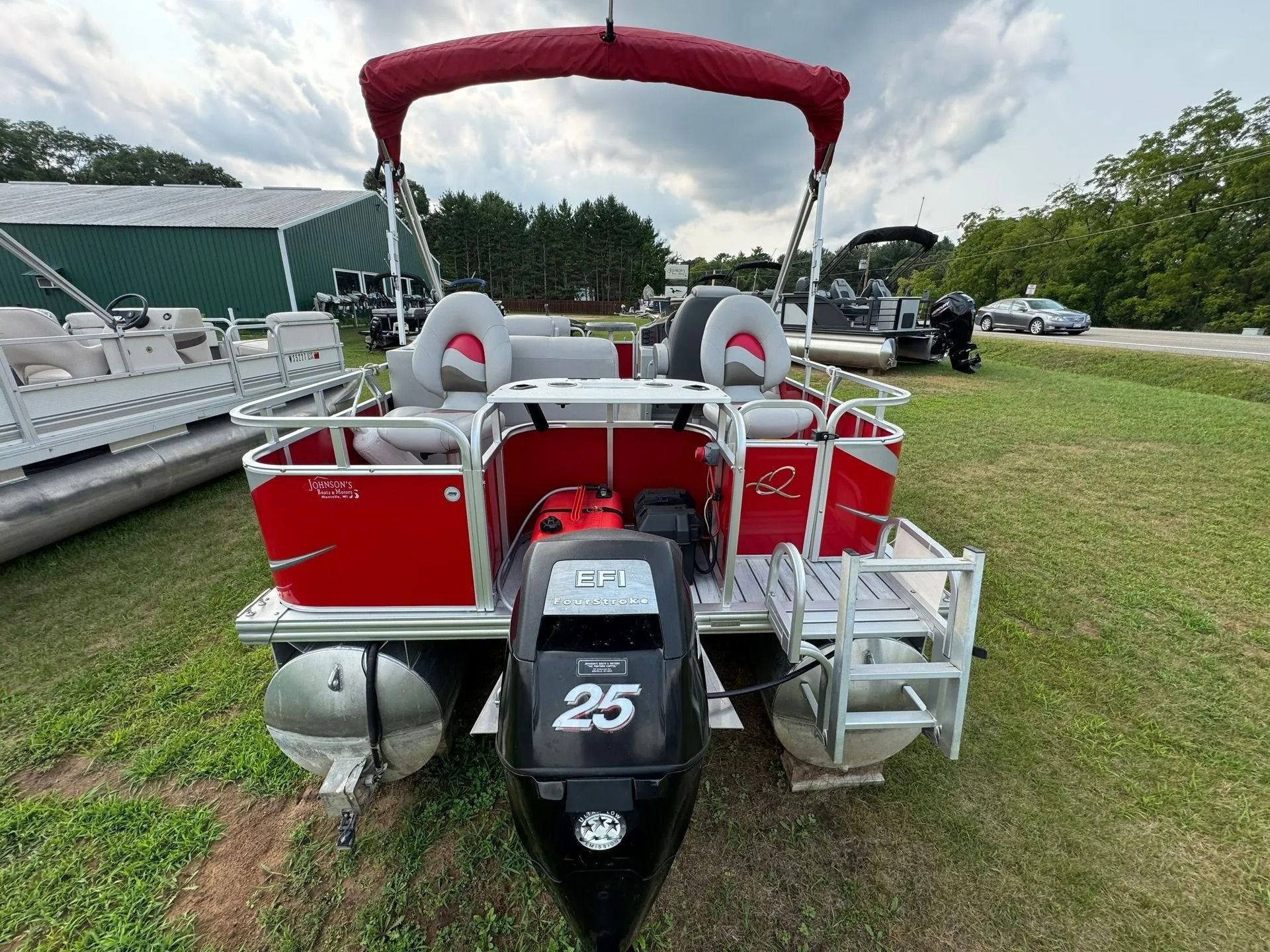 Red pontoon boat with gray seats and black 25 HP motor parked on grass beside a dock