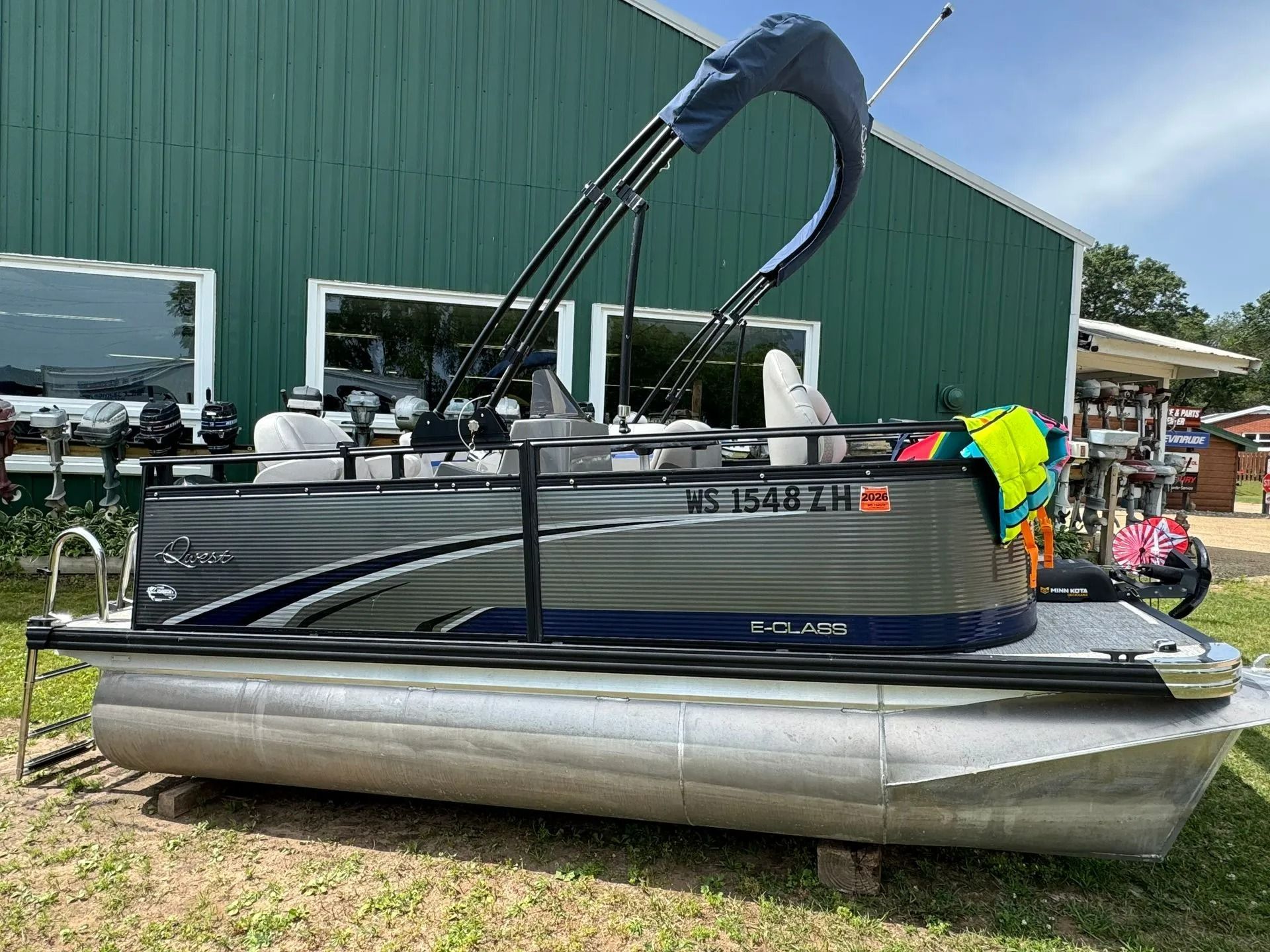 Pontoon boat with black canopy parked on grass outside a green building