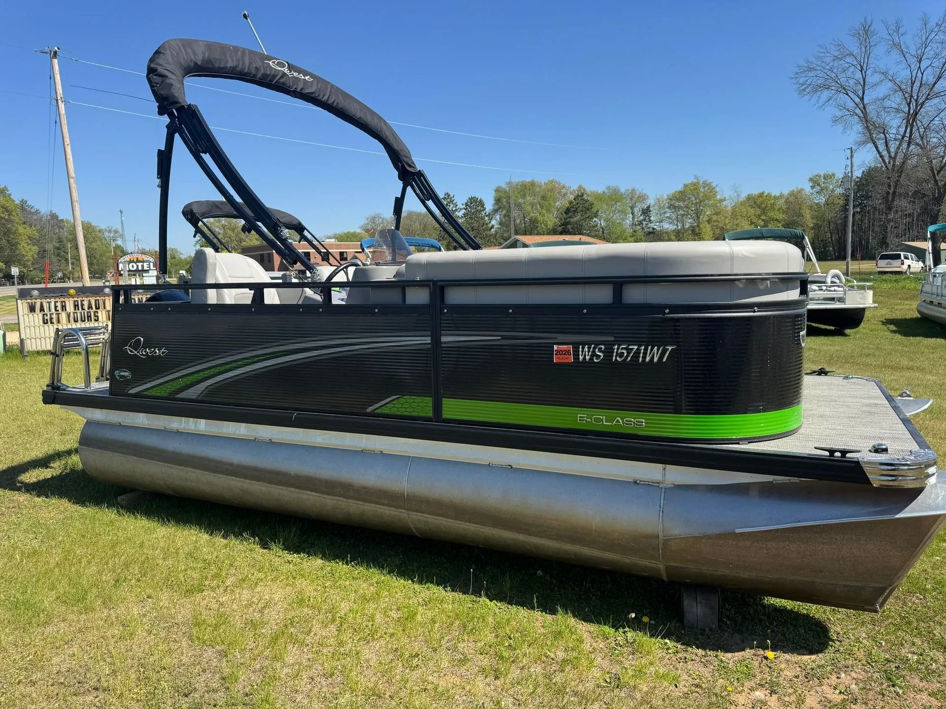 Pontoon boat with black and gray sides on a grassy shore under a clear blue sky