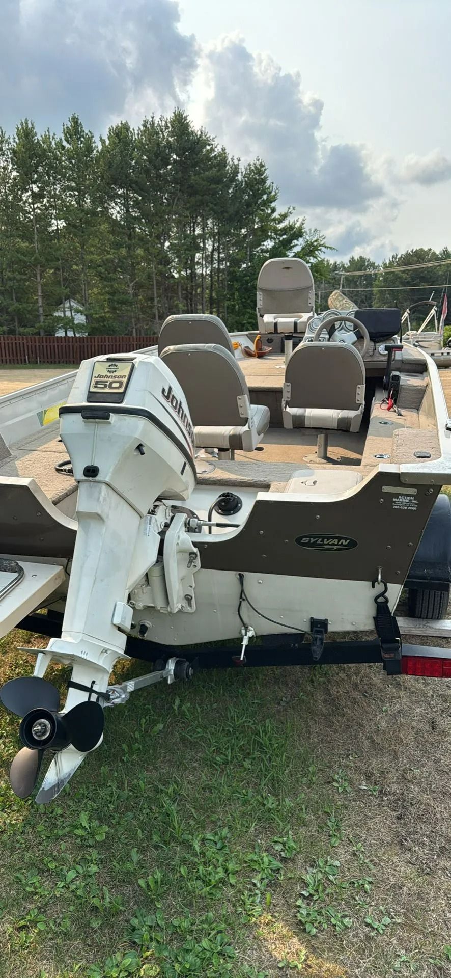 White outboard motor on a bass boat parked on grass under a cloudy sky with trees behind.