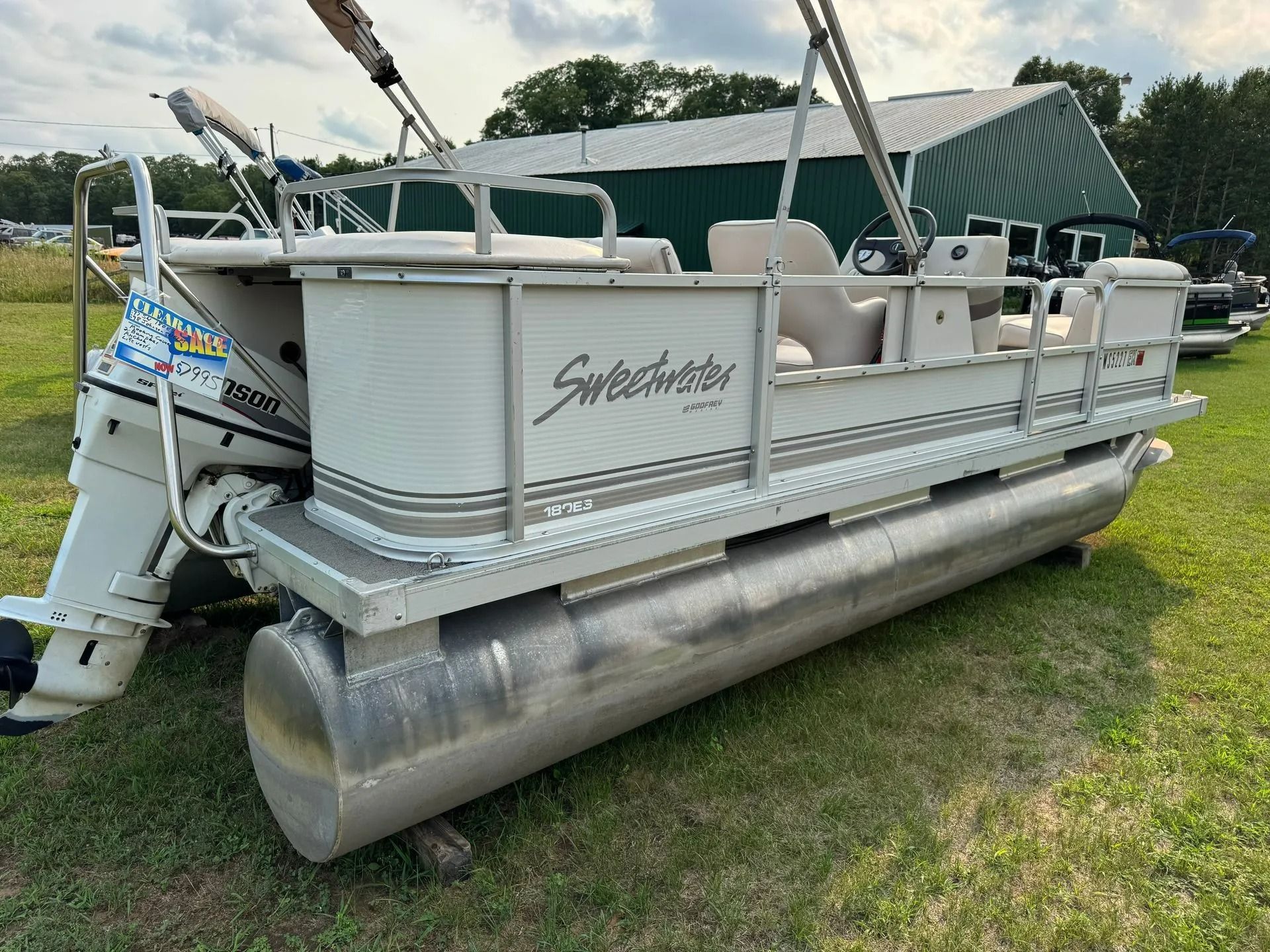 Pontoon boat with gray railings and covered seating, parked on grass under a canopy.