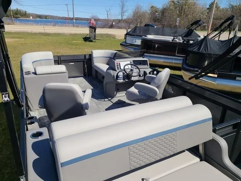 Pontoon boat with gray seats and steering console docked on a grassy shore near water