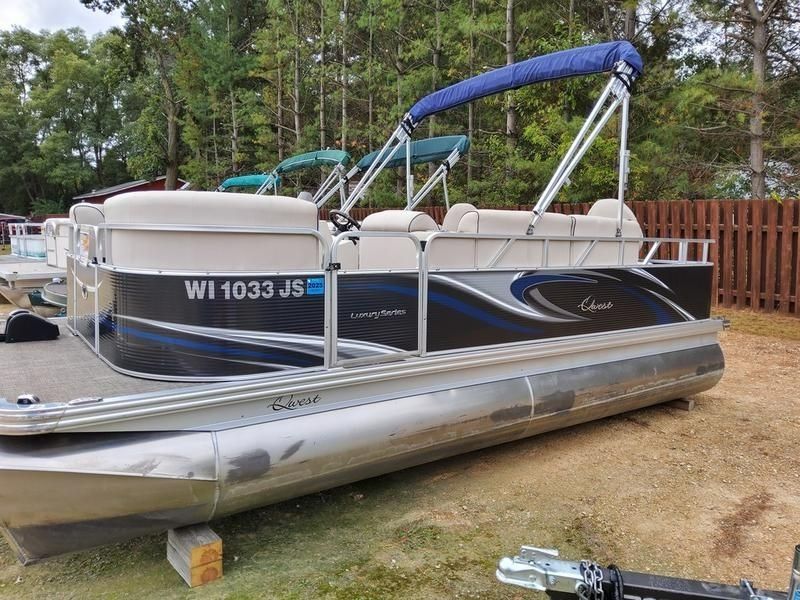 Pontoon boat on a trailer at a wooded campsite, with blue canopy and Wisconsin registration number.