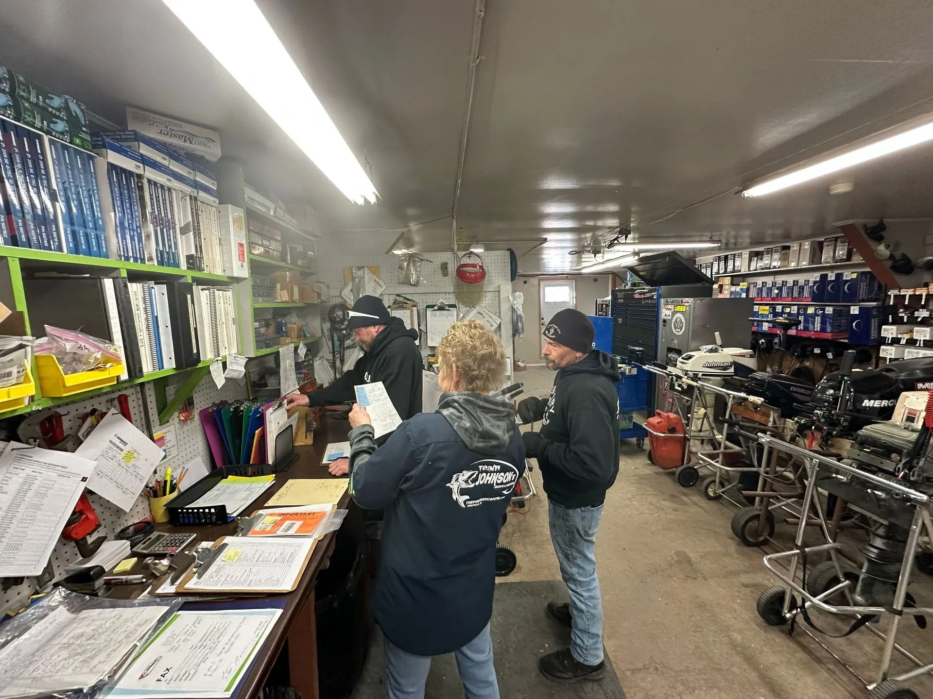 People browsing a cluttered retail shop with shelves of goods and carts in a narrow aisle