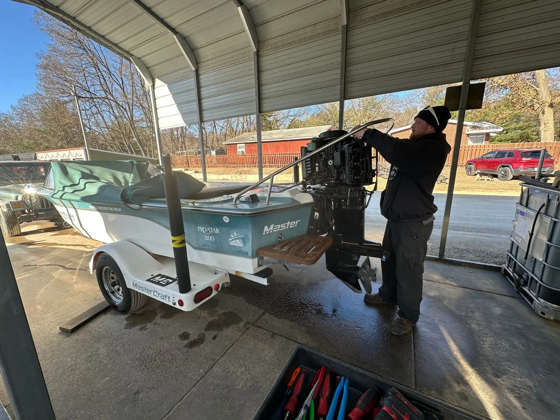 Person washing a small teal boat on a trailer under a covered dock area