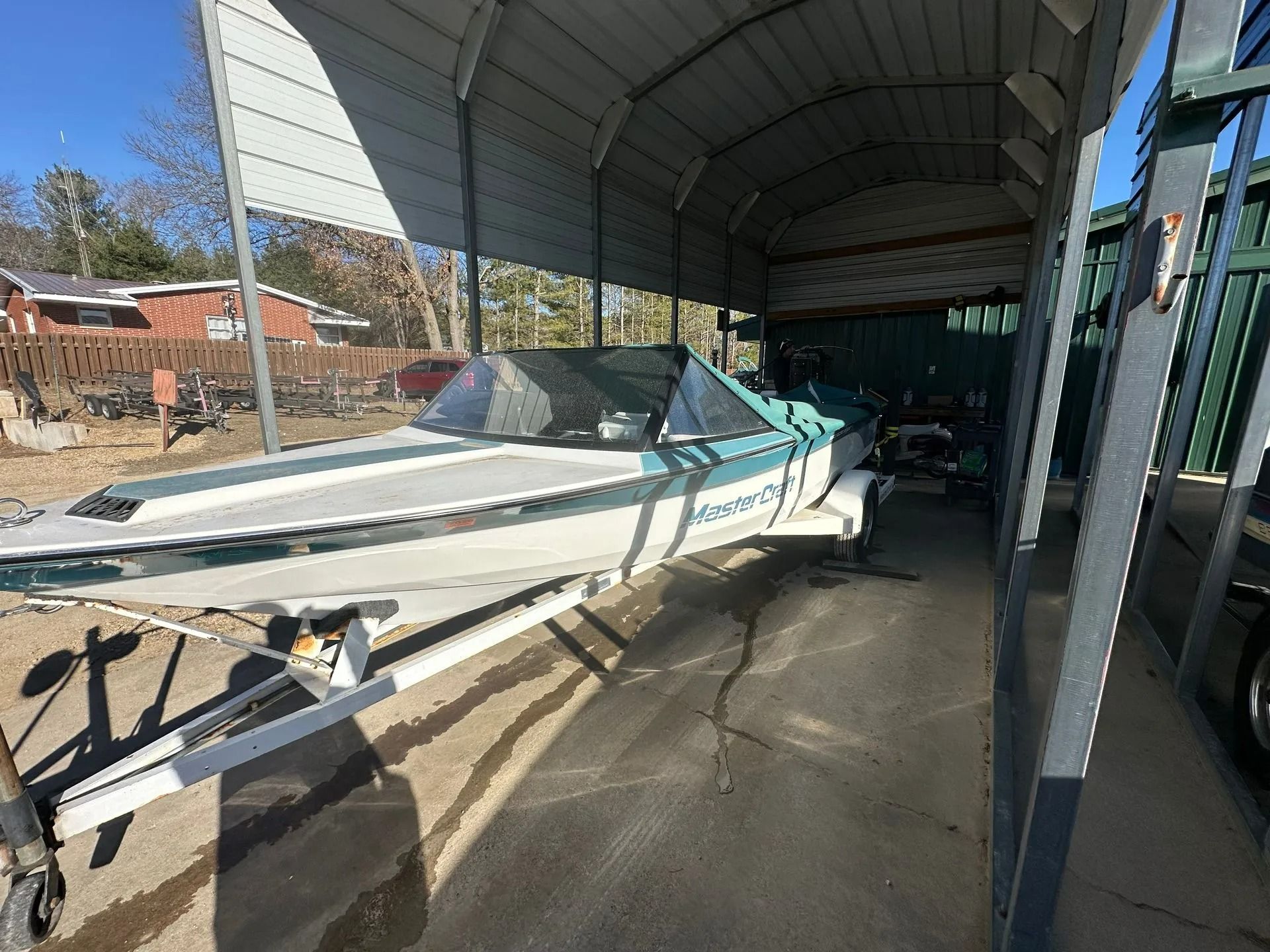 White speedboat on a trailer parked under a covered shed, with another boat inside the storage area.