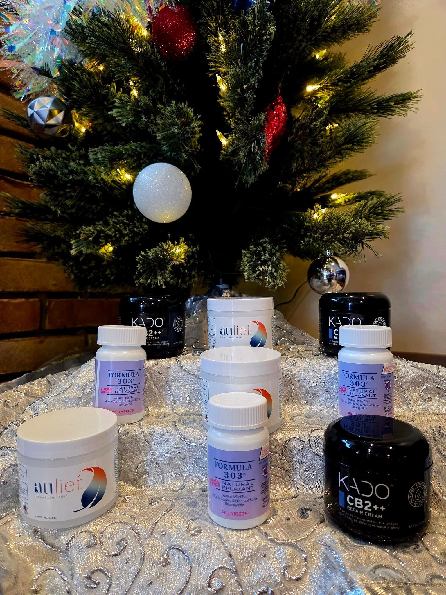 Several supplement jars are displayed on a white, sparkly surface in front of an illuminated Christmas tree.