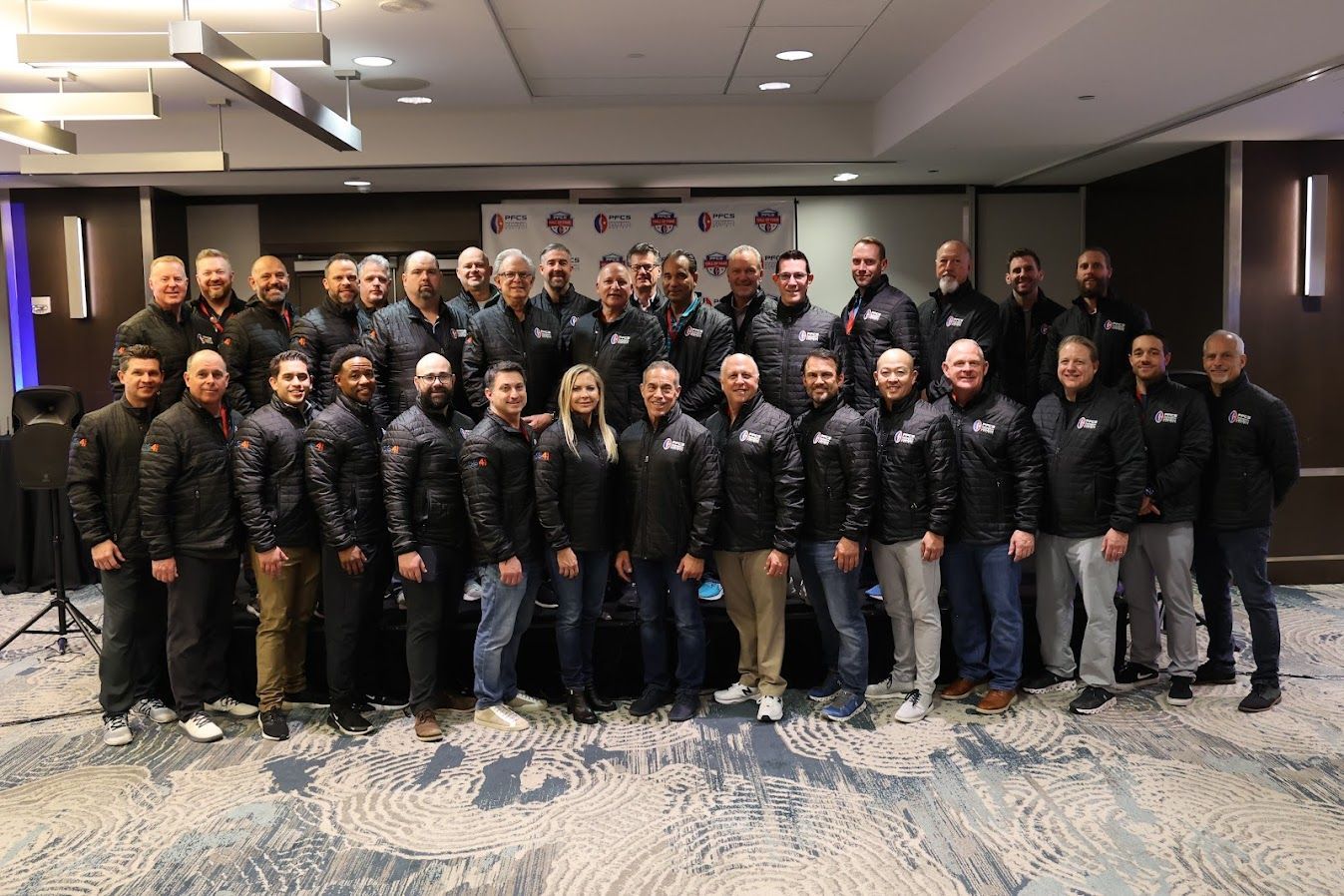 Large group of people in black jackets posing together in a hotel conference room