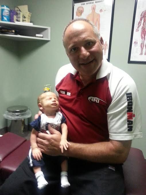 A person in a maroon and white shirt holds a newborn in a clinic with anatomical charts on the wall.