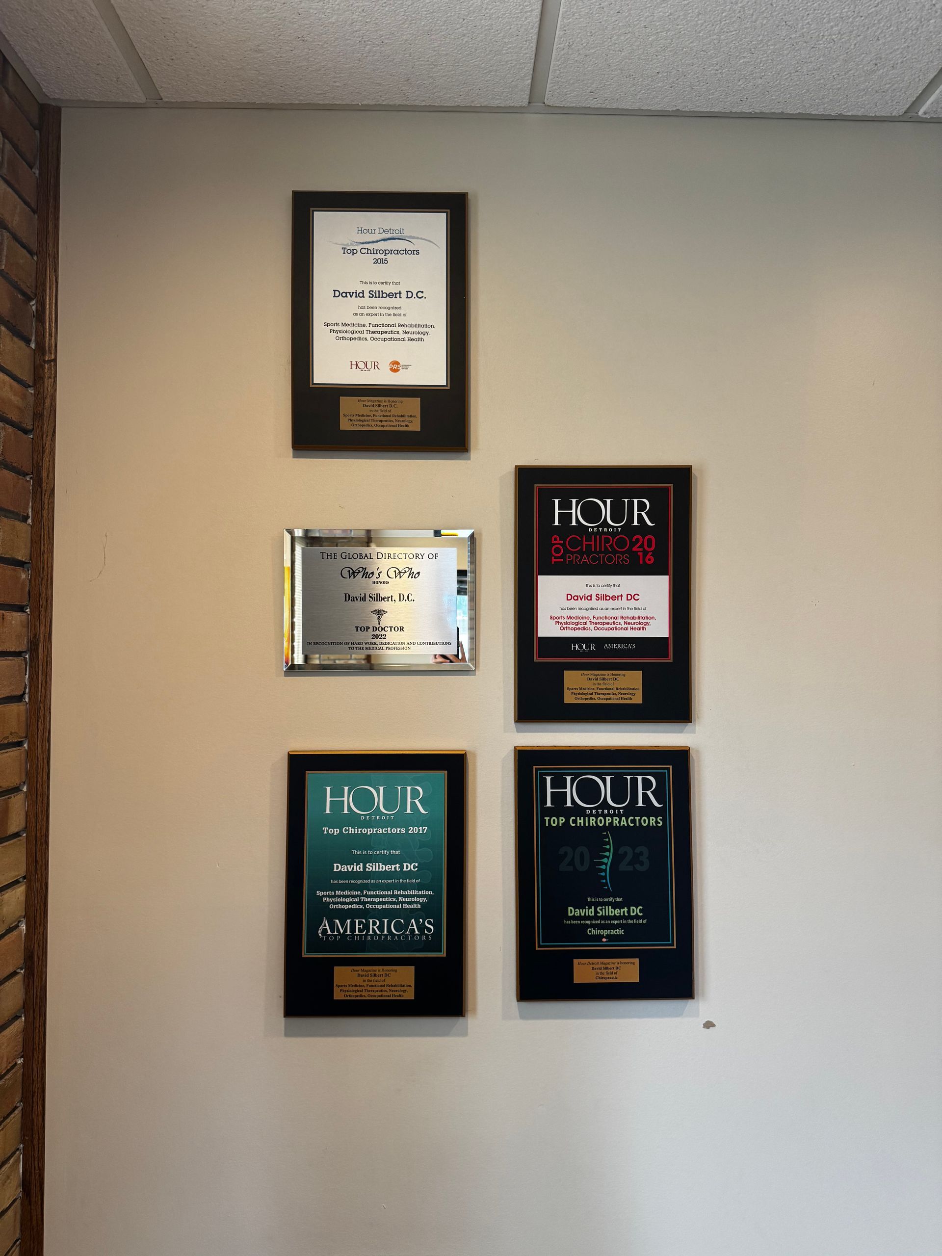 Five awards mounted on a light gray office wall, featuring four black frames and one silver metallic plaque.
