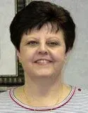 A person with dark, short hair smiles while wearing a white shirt with thin horizontal blue and red stripes.