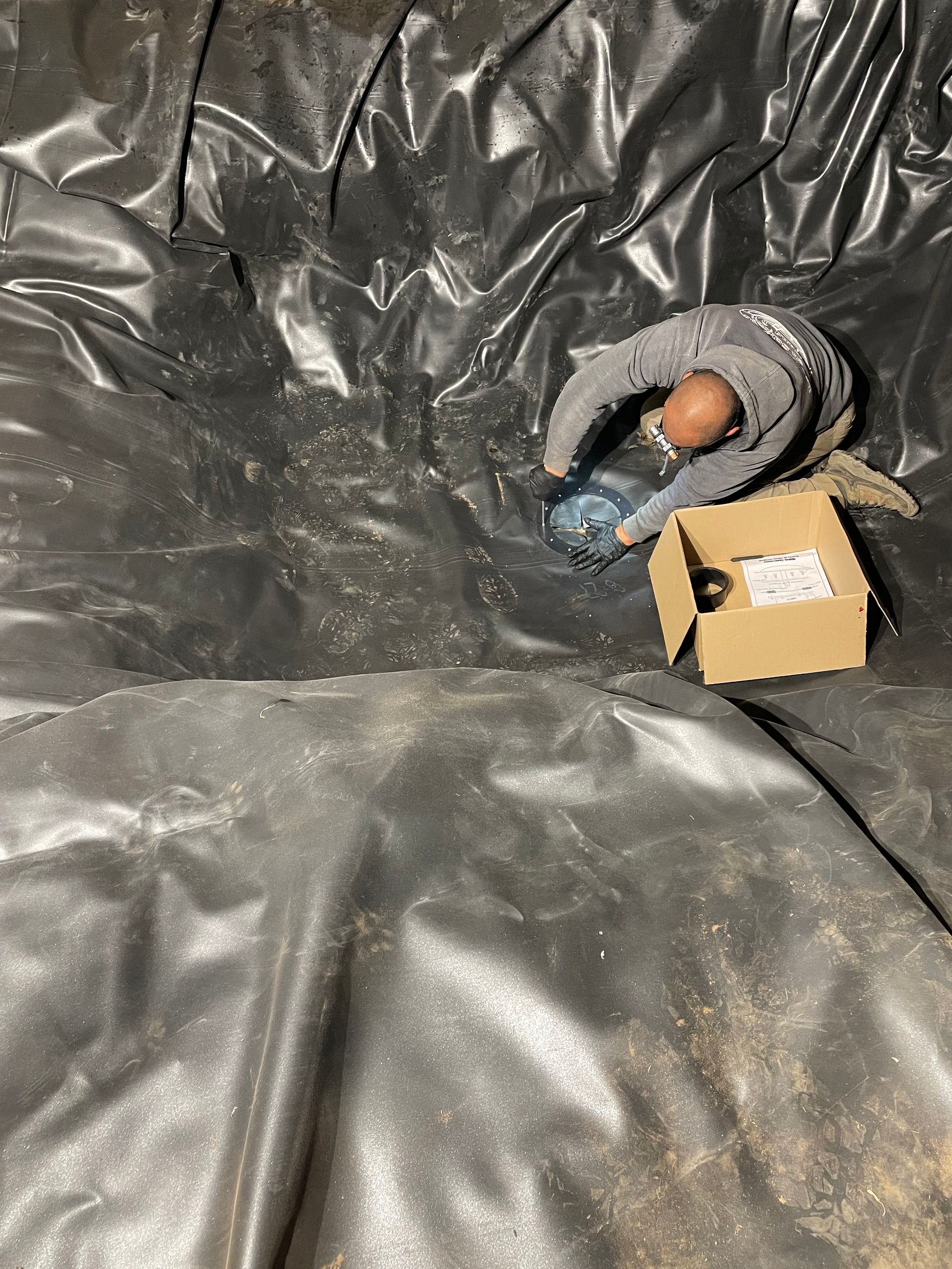 Small doll in gray blanket beside a small cardboard box on a black tarp backdrop