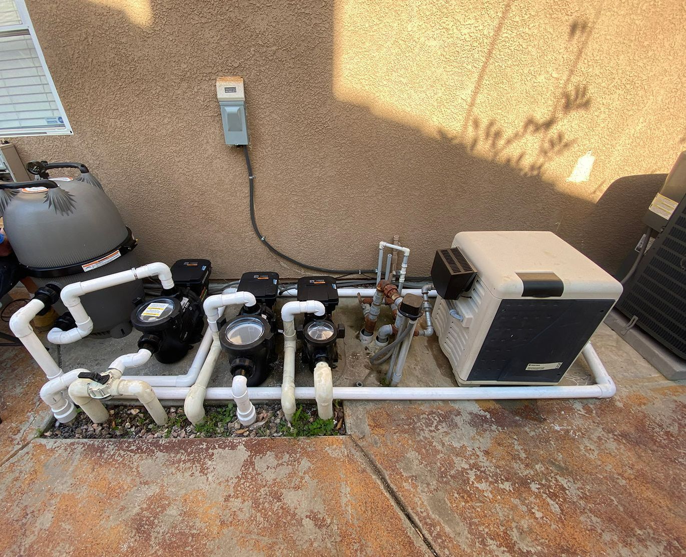 A swimming pool pump is sitting on a concrete surface next to a wall.
