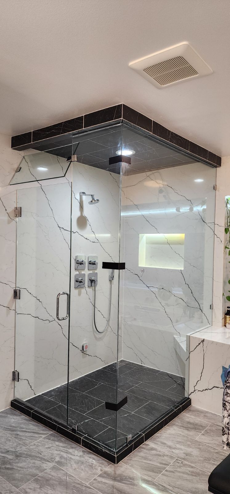 Modern, glass-enclosed shower with black marble base and white marble patterned walls.