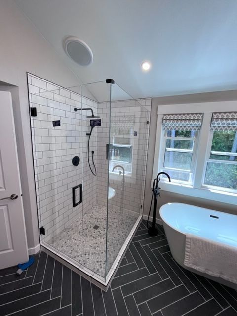 Modern bathroom with glass shower, subway tile, black fixtures, and freestanding tub.