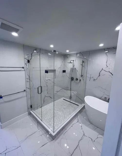 Modern bathroom with marble-patterned tile, glass shower, and a white tub.