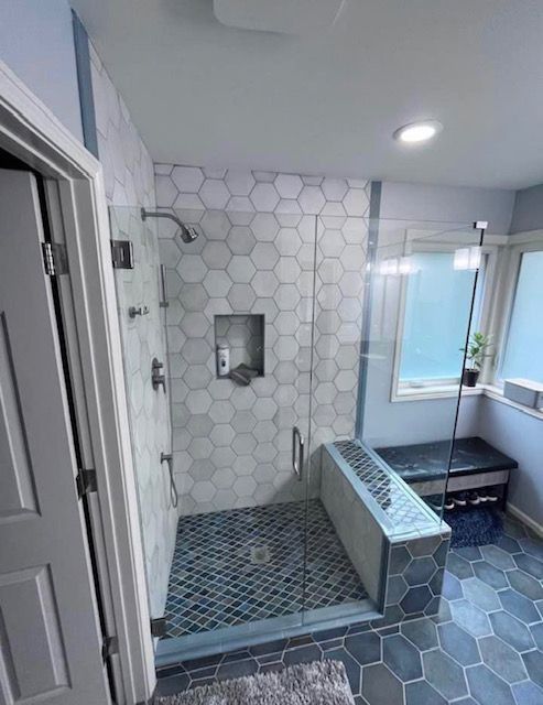 Modern bathroom with blue and white hexagonal tiles, glass shower, and a bench.