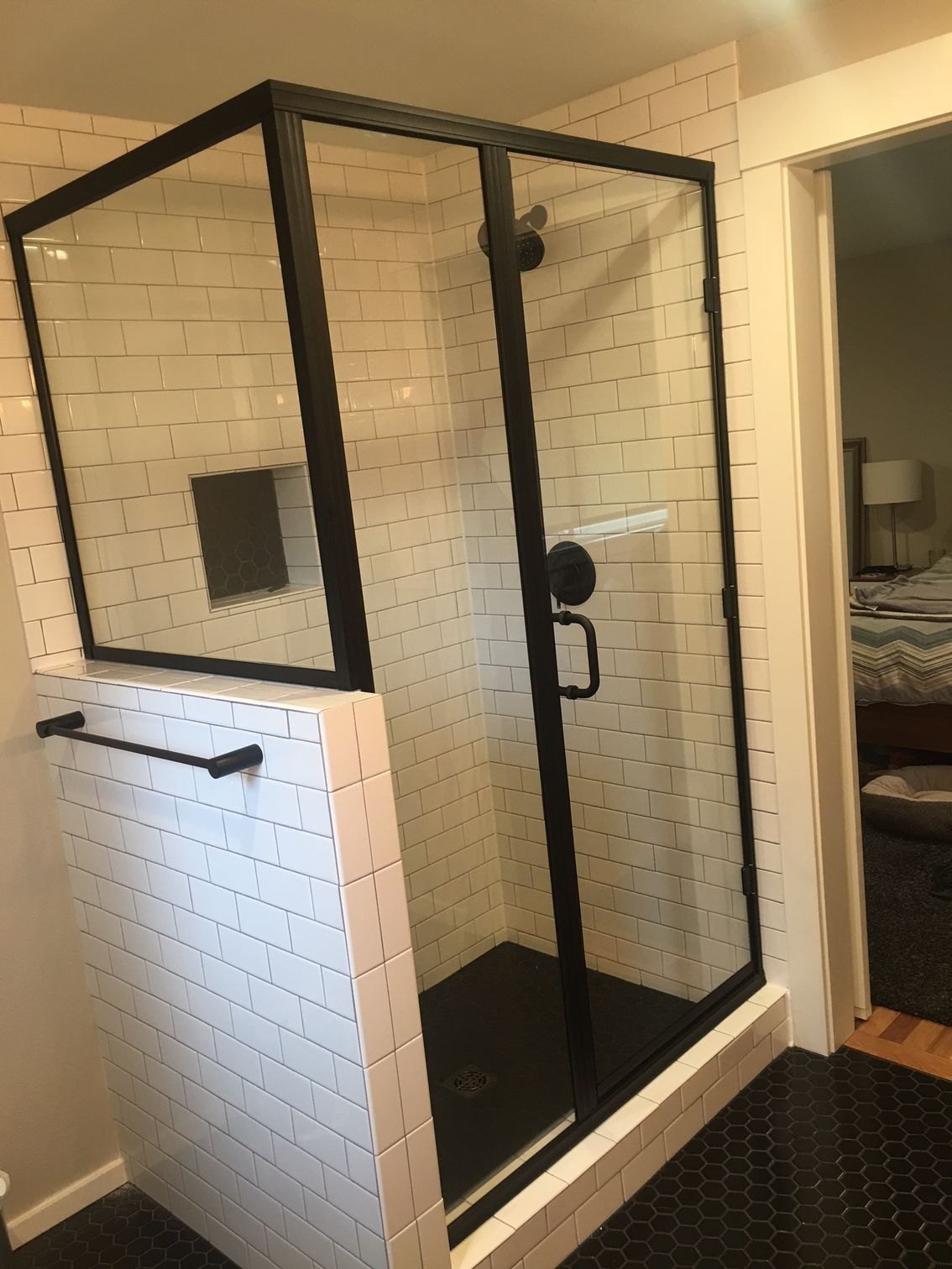 Black-framed glass shower with black fixtures, subway tile, and black tiled floor.