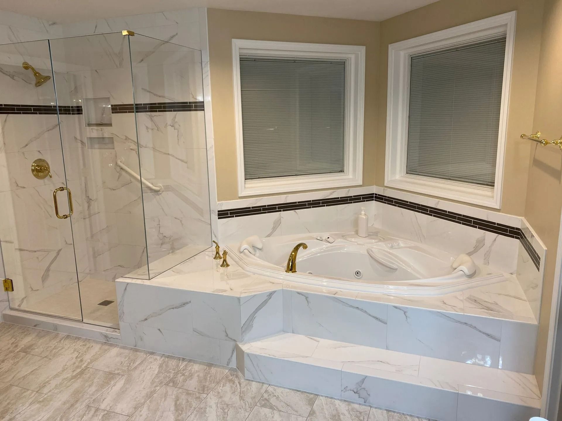 Luxurious bathroom with white marble tiles, glass shower, and jacuzzi tub. Golden fixtures.