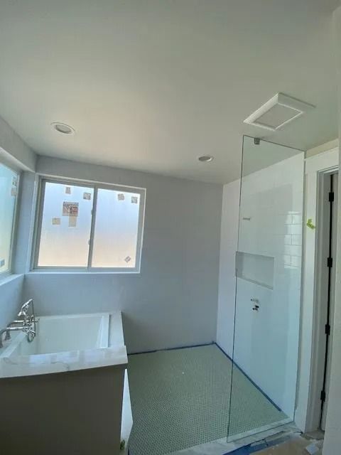 Bathroom with tub, shower, and window, light green floor tiles, white walls.