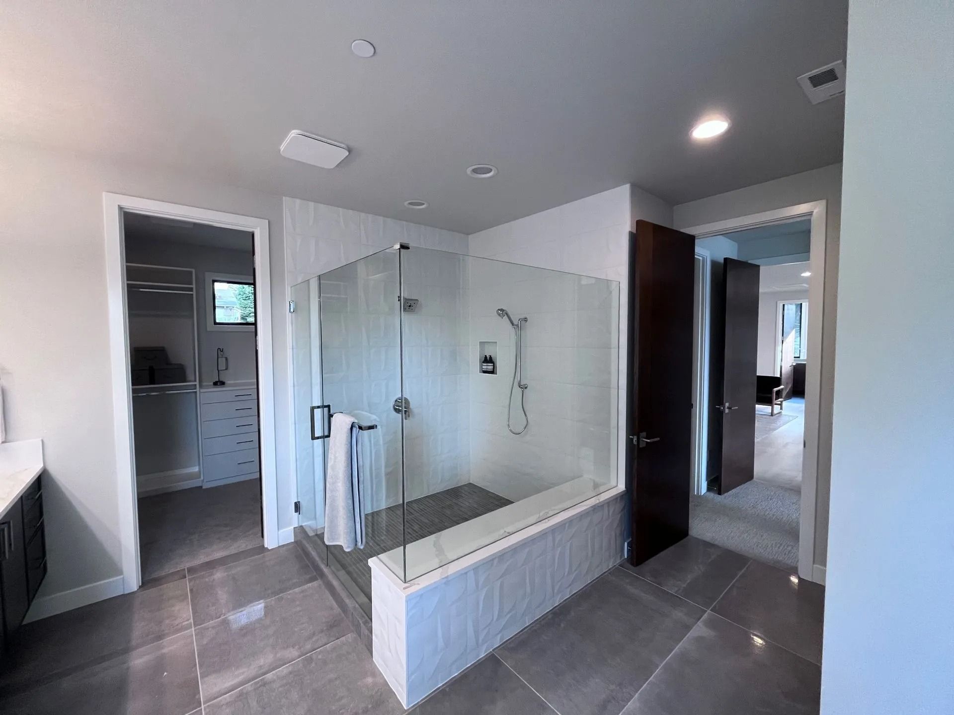 Bathroom with a glass shower, walk-in closet on the left, and a doorway to a bedroom on the right.