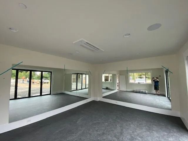 A yoga or dance studio with mirrored walls, windows, and dark floor, with someone standing near a window.