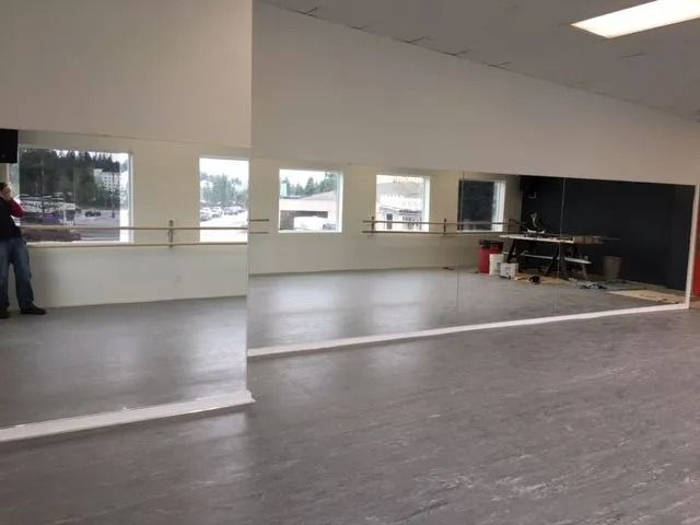Dance studio with large mirrors, windows, and barre. A person stands near the edge.