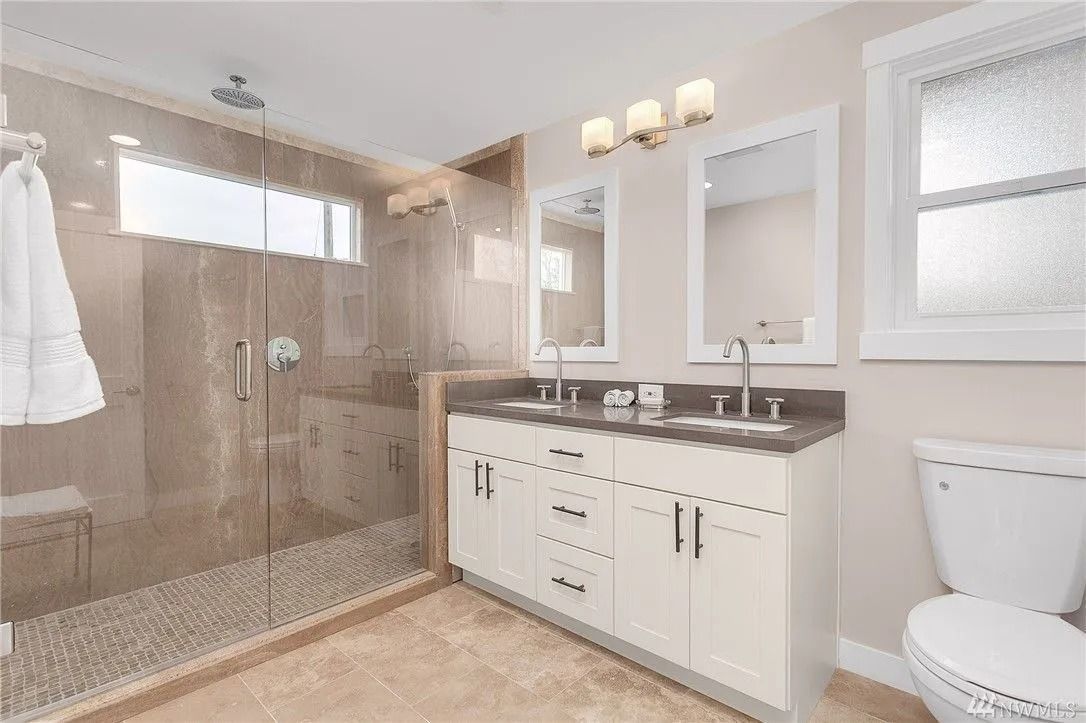 Modern bathroom with glass shower, double vanity, and toilet.