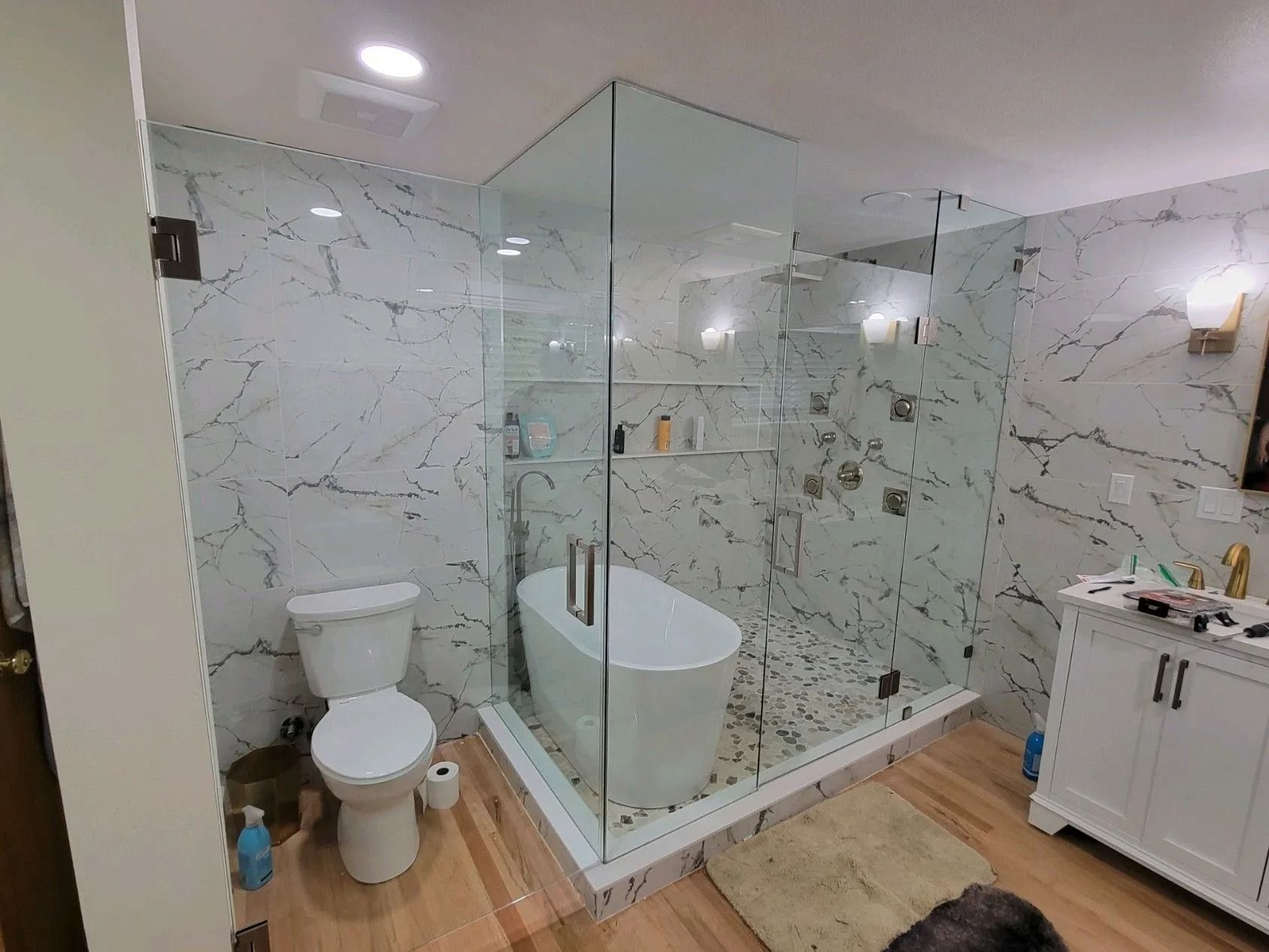 A modern bathroom with white marble walls, a glass shower, a freestanding tub, and a white vanity.