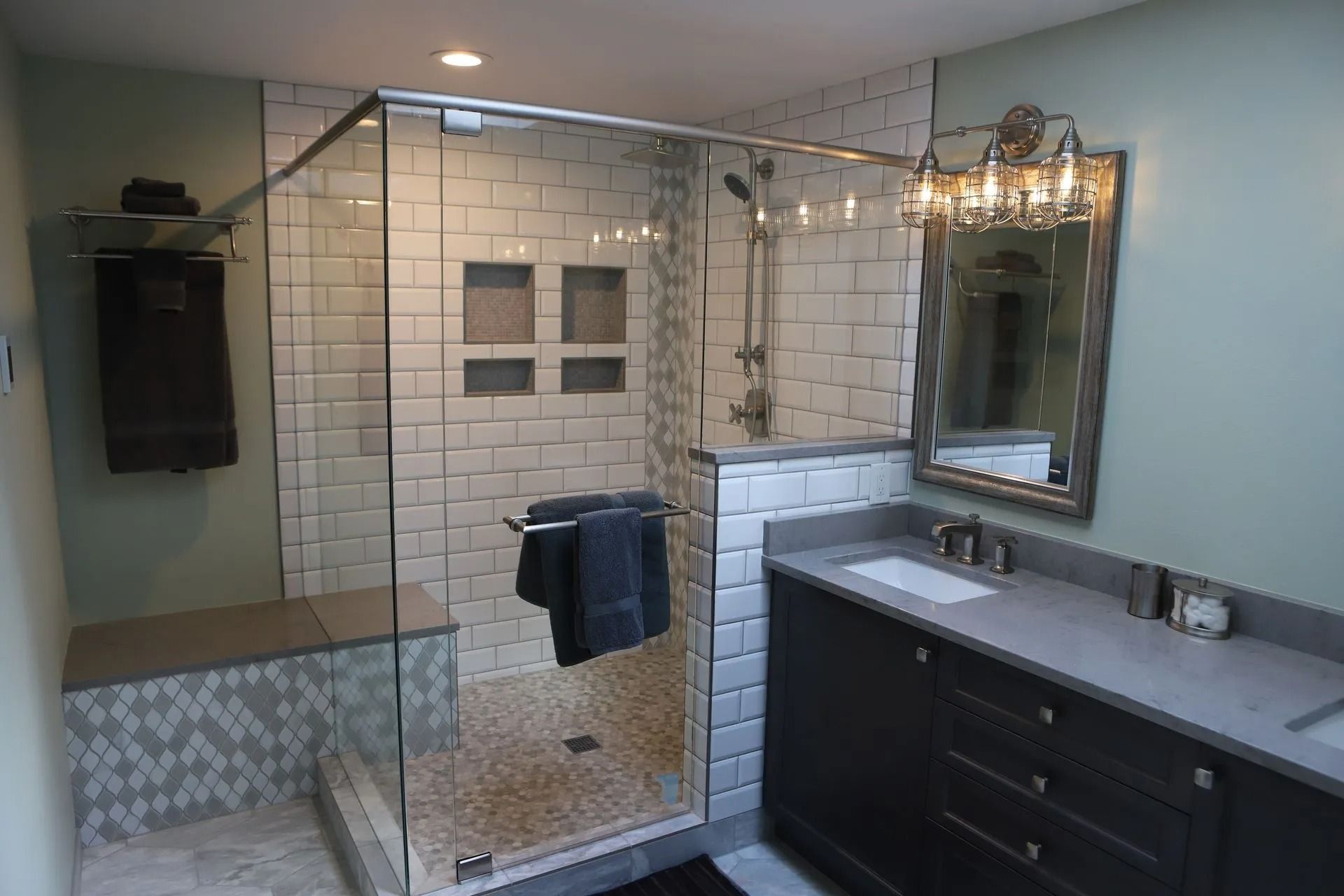 Bathroom with a glass-enclosed shower, dark vanity, and gray countertops. Shower has a built-in bench and niche.