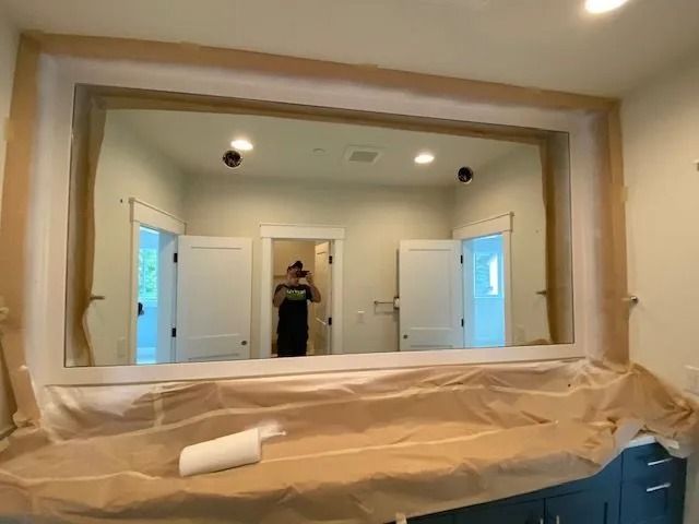 Bathroom mirror framed by light wood, reflecting doors and a person in the center. Beige paper covers the vanity.