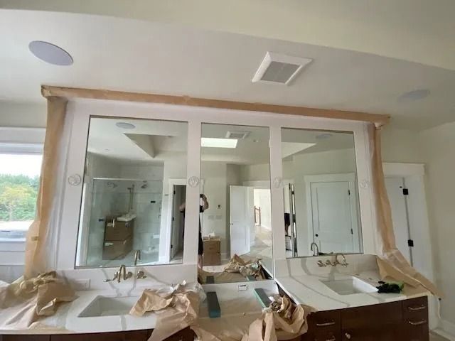 Bathroom with three mirrors over a vanity, fixtures with brown paper protection, white walls, and a skylight.