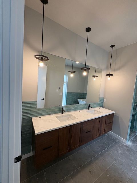 Modern double-sink bathroom vanity with dark wood cabinets, white stone countertop, blue tile backsplash, and pendants.