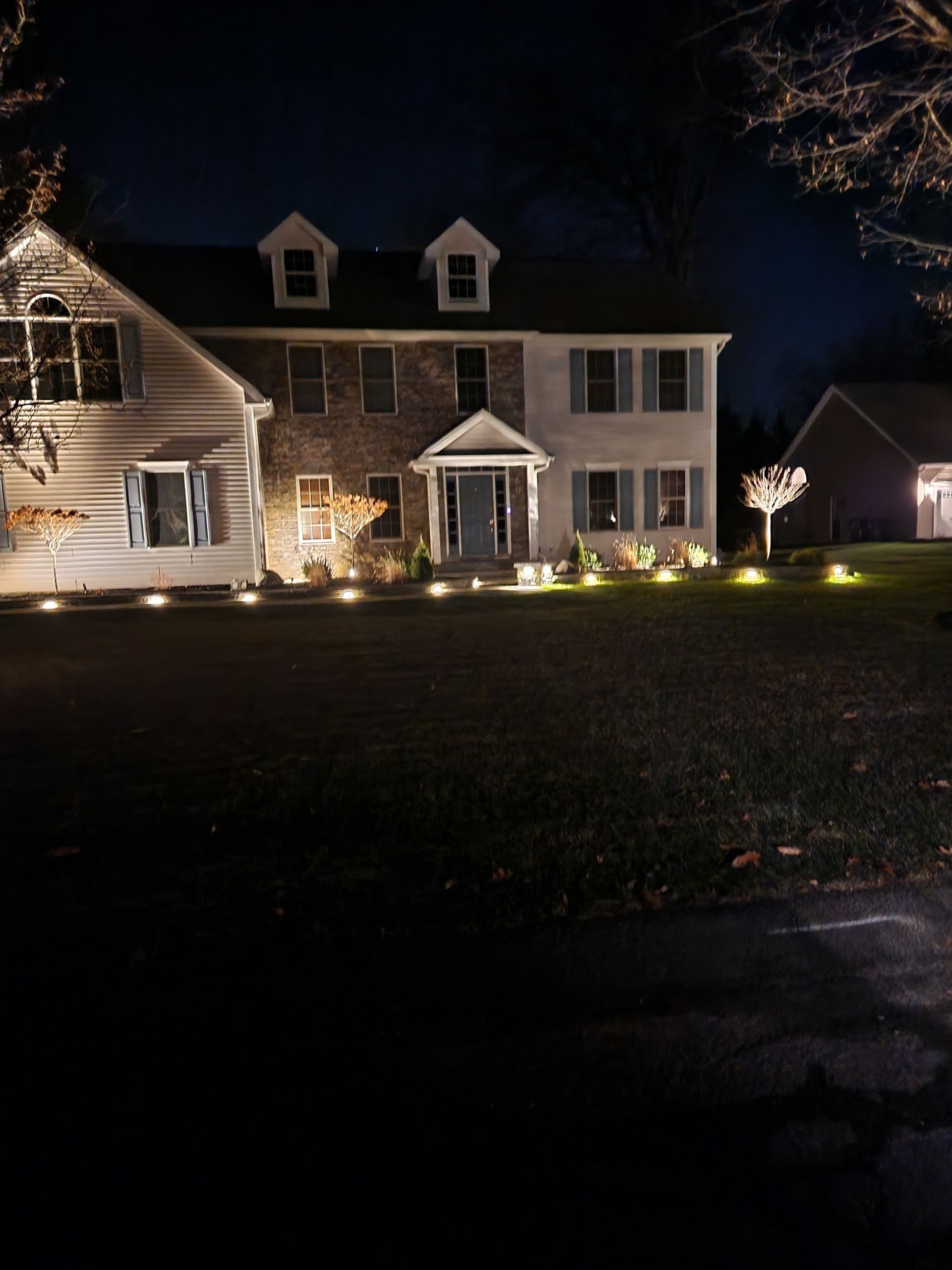 A two-story house with landscape lighting at night. Brick and siding exterior.