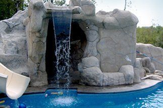 Pool with waterfall feature and slide. Light-colored rock structure with water cascading into the blue pool.